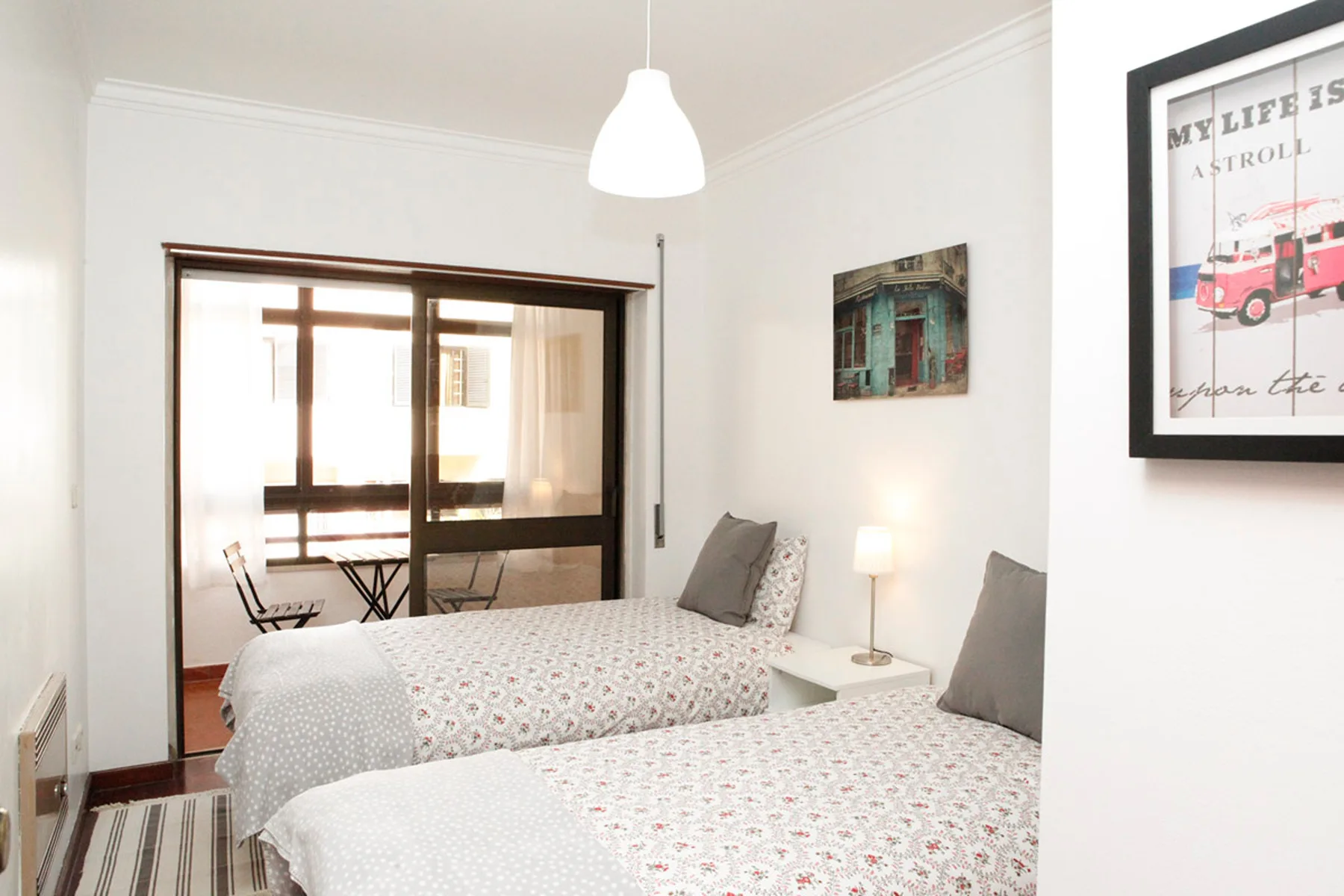 Un dormitorio luminoso con dos camas, mesillas y cuadros en la pared.