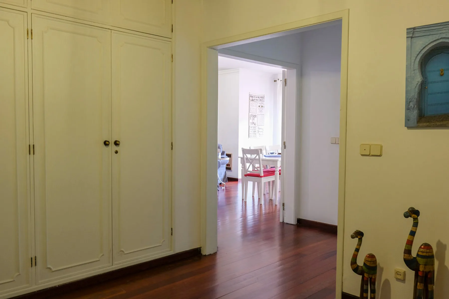 Un pasillo interior da a un comedor luminoso con suelo de madera.