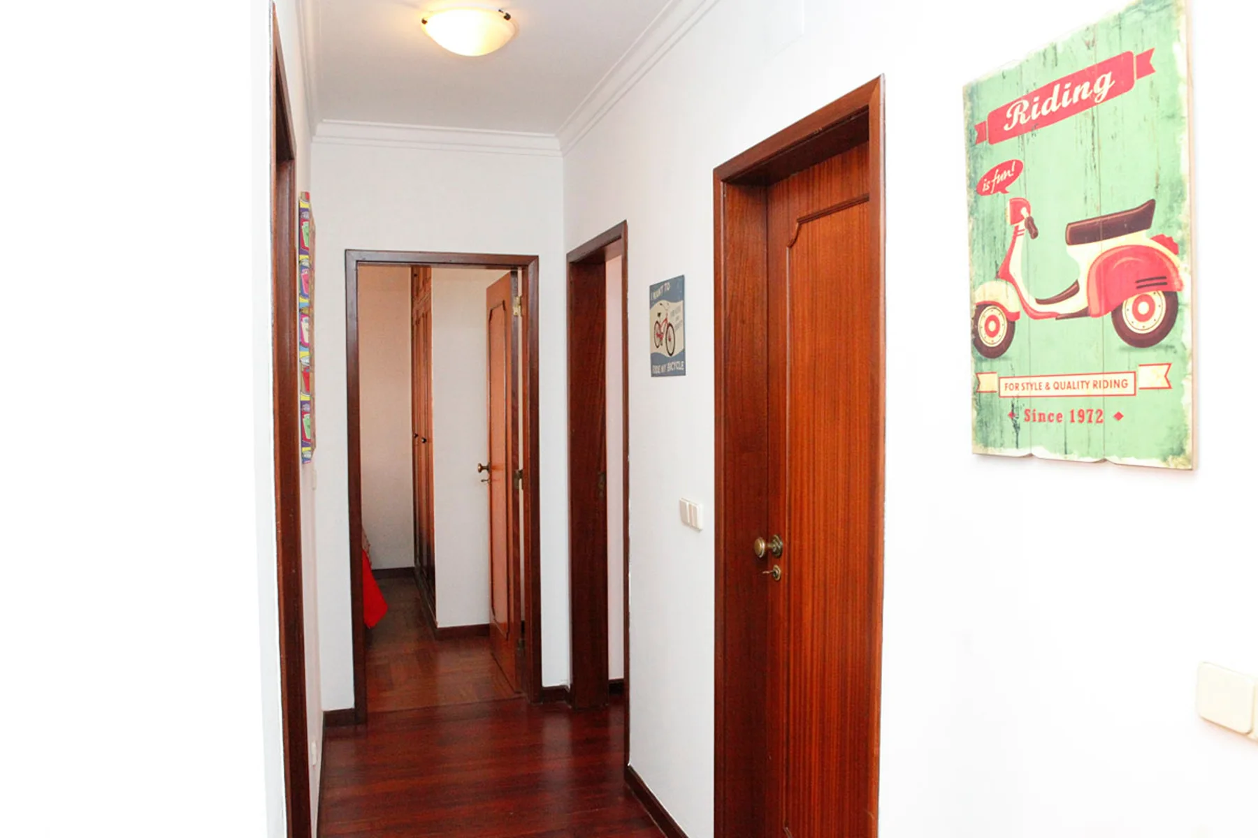 Un pasillo de paredes blancas con puertas de madera y un póster enmarcado de estilo vintage.