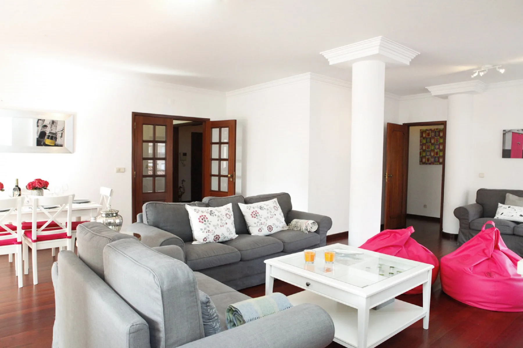 Una sala luminosa tiene asientos grises, una mesa de centro blanca y pufs de colores.