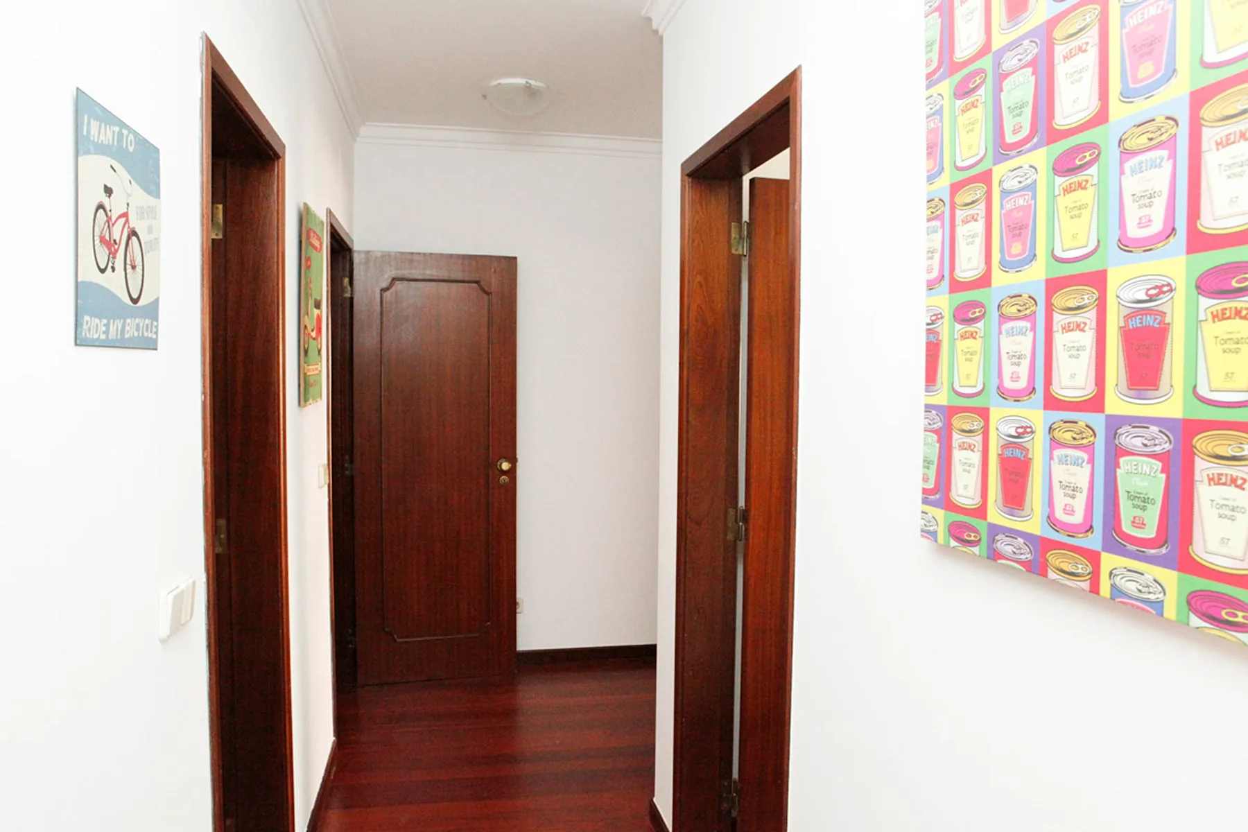 Un pasillo con puertas de madera oscura y cuadros coloridos.