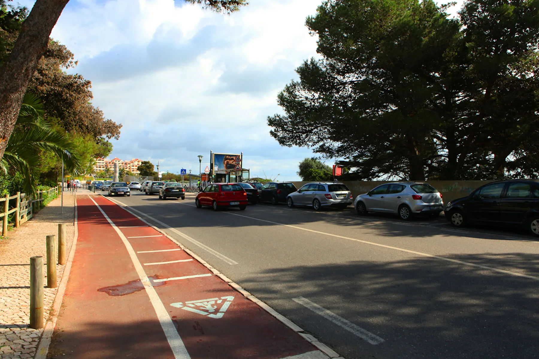 Una carretera arbolada con un carril bici rojo y coches aparcados.