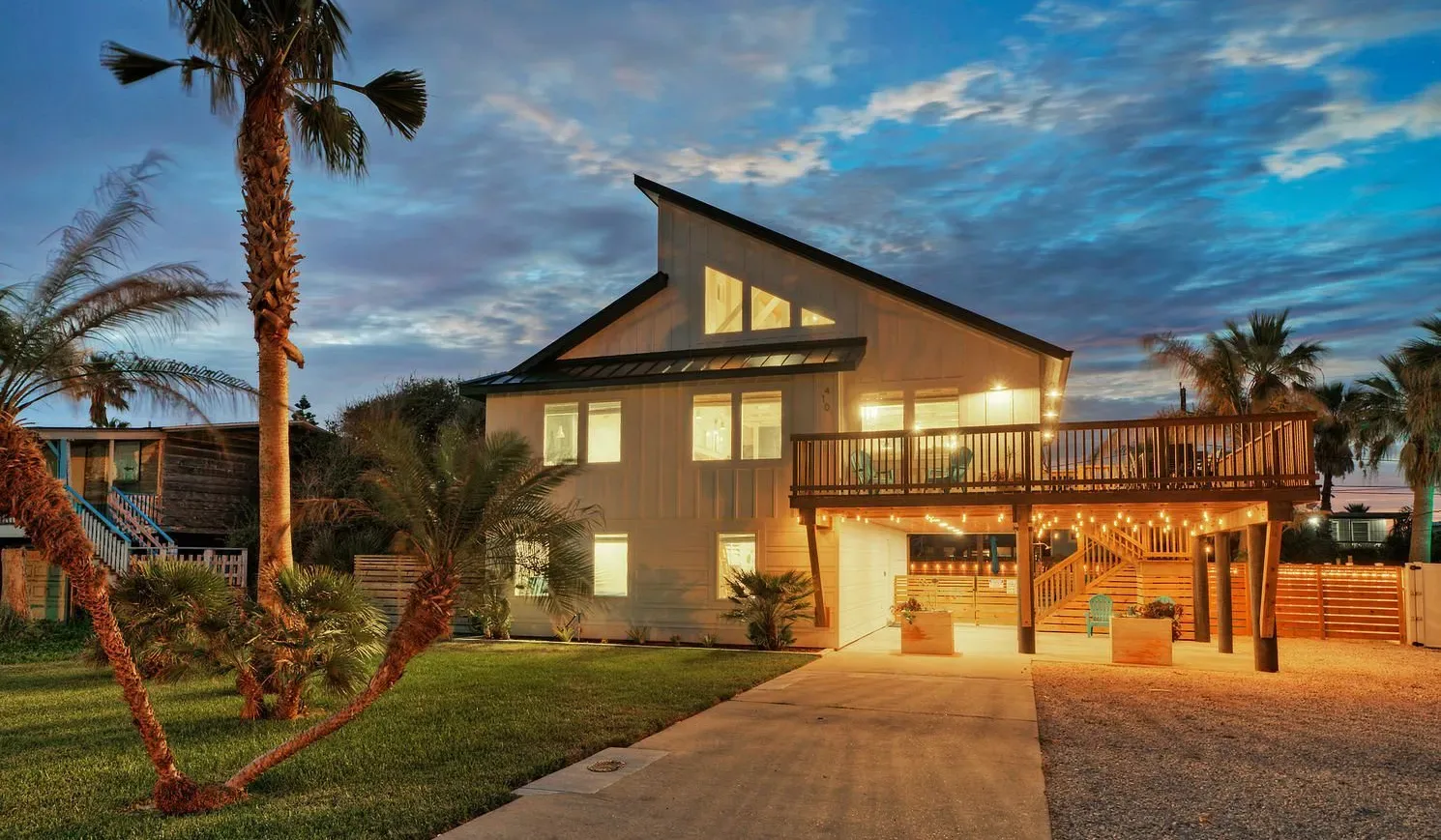 A modern house glows at dusk, with a broad driveway leading to its entrance.