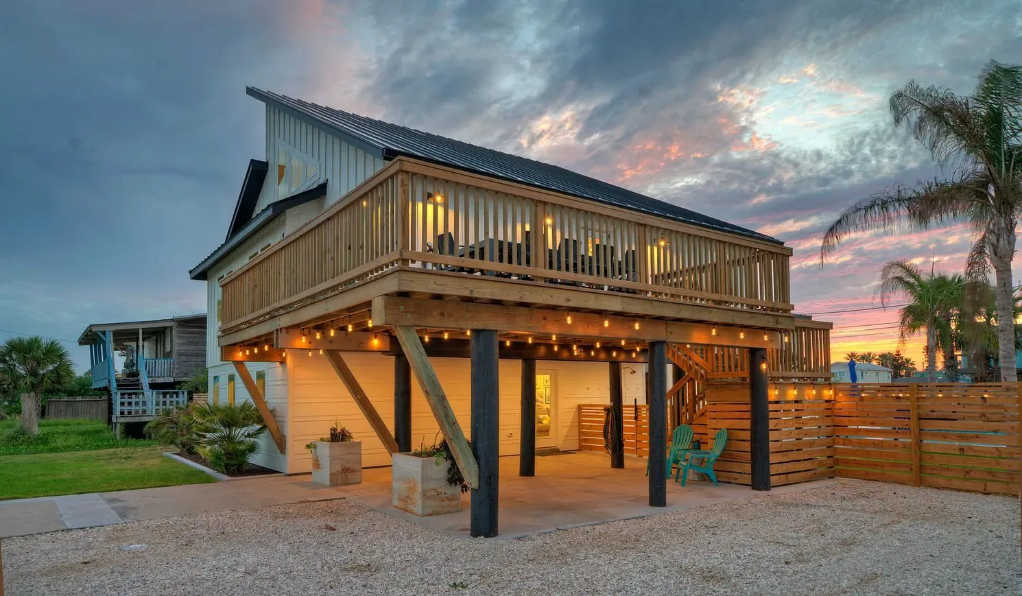 An elevated coastal-style home with a wooden deck glows at sunset.