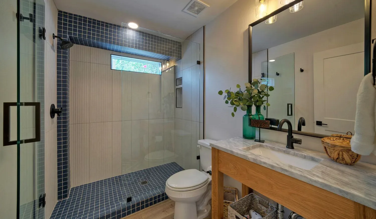 A bathroom with a glass shower and a vanity topped with a mirror.