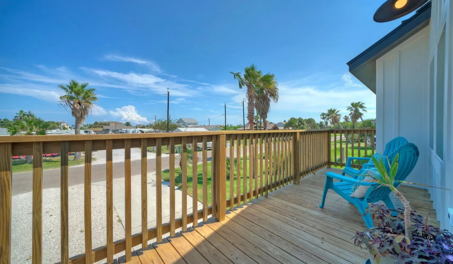 A wooden deck overlooks a sunny outdoor area, with blue seating beside the wall.