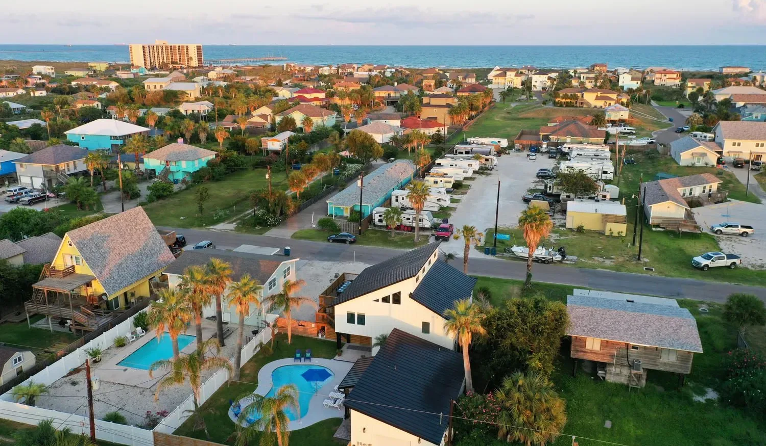 Aerial view of a coastal neighborhood with homes, roads, and the sea beyond.