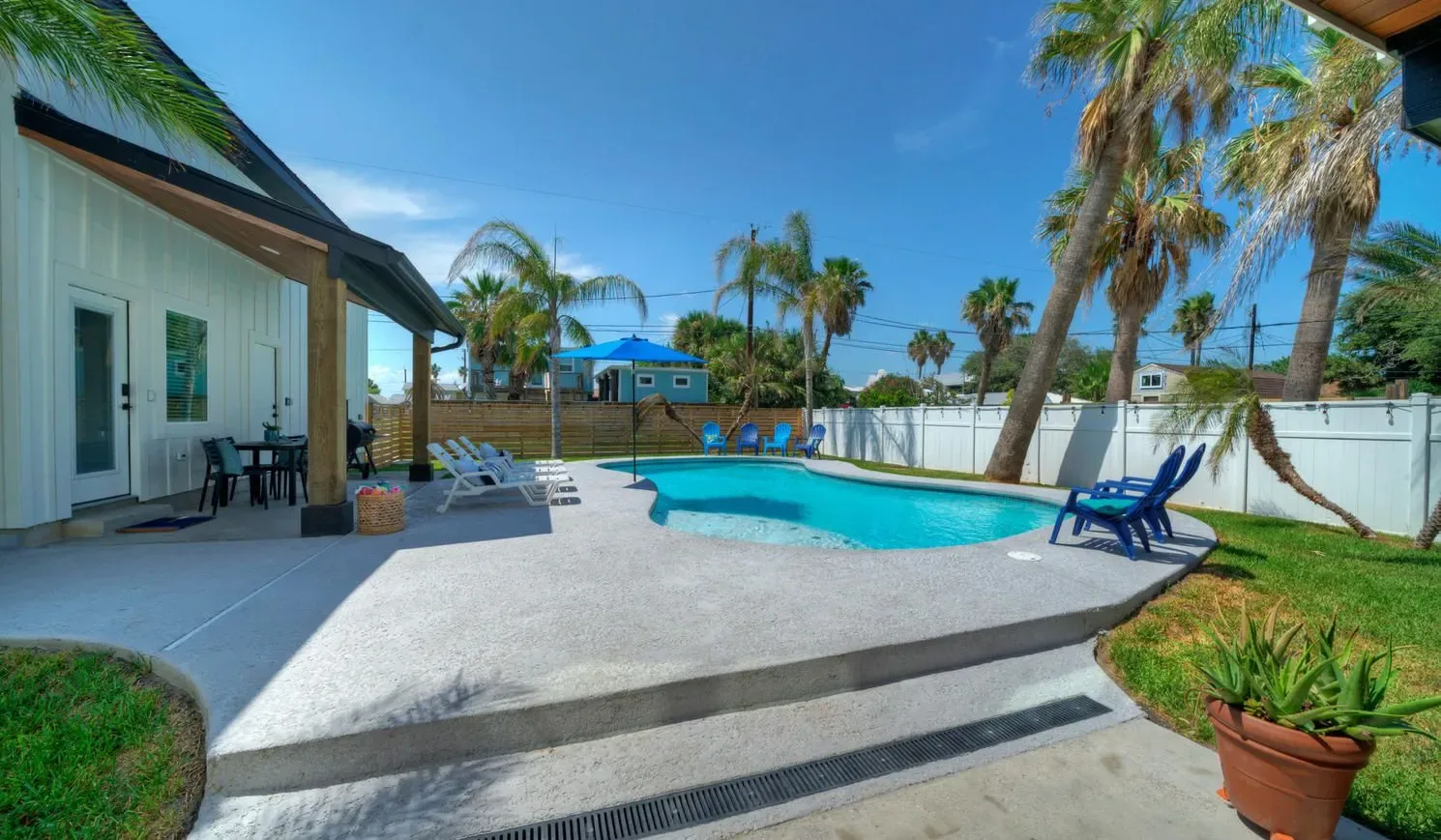 A sunny outdoor pool area with patio seating and palm trees.
