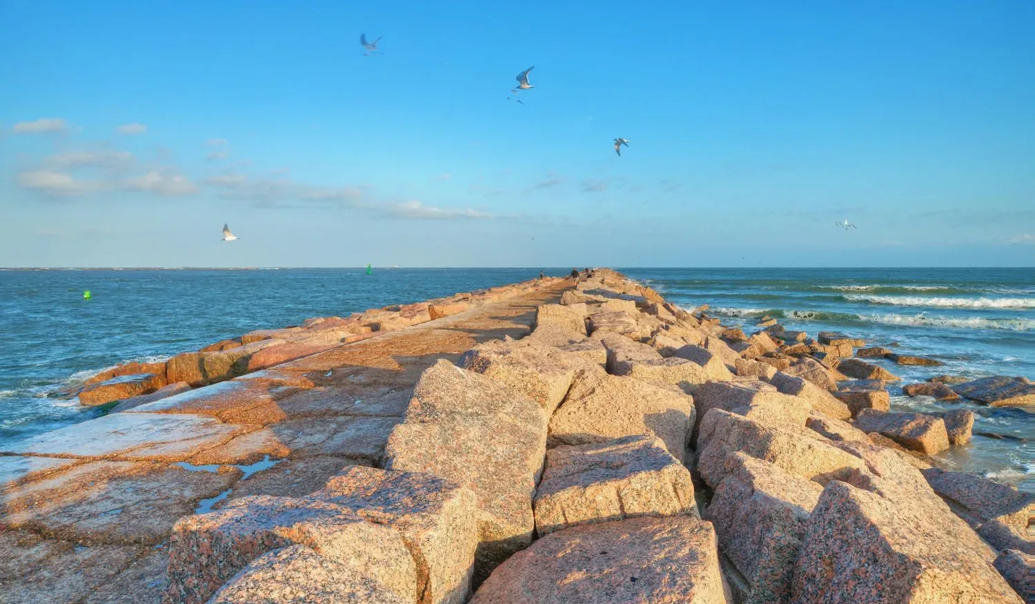 A rocky shoreline extends into the sea beneath a clear blue sky.