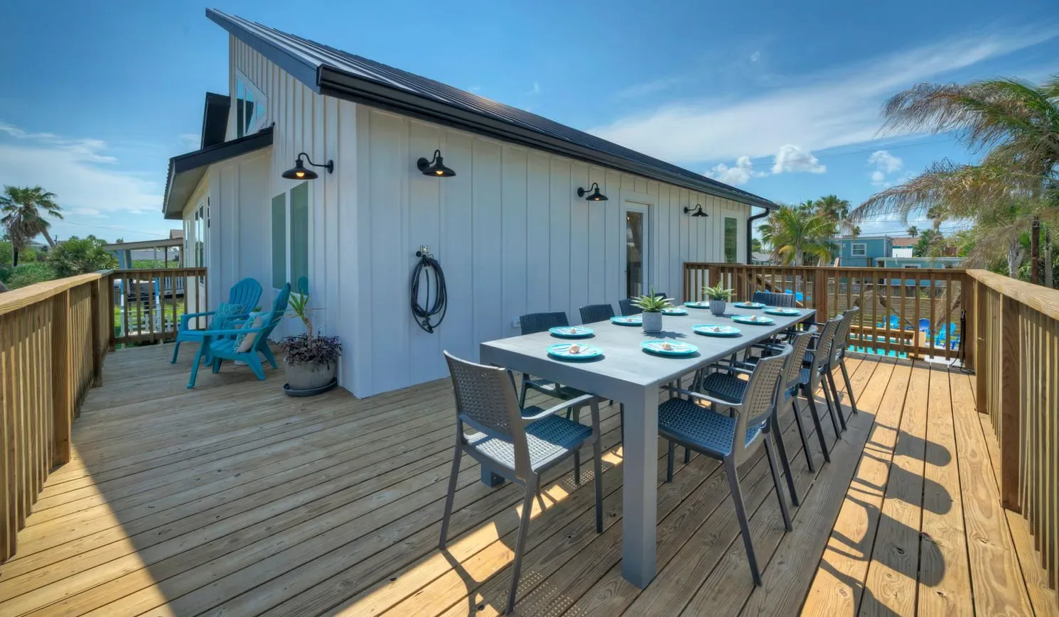 A rooftop deck has an outdoor dining table and seating beside a white building.