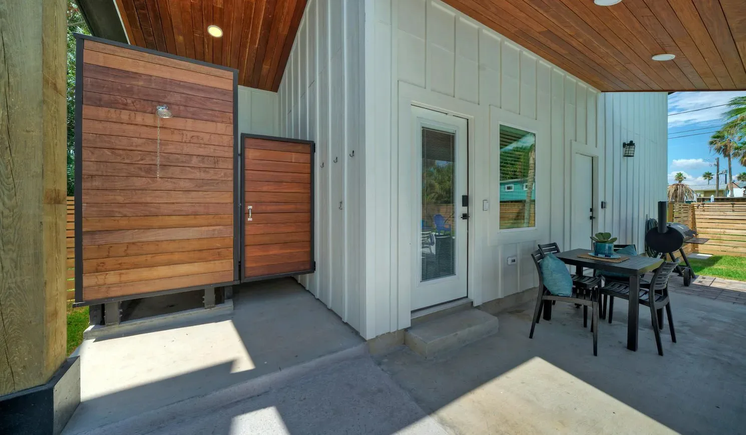 A covered patio with a dining table beside a white-sided building.