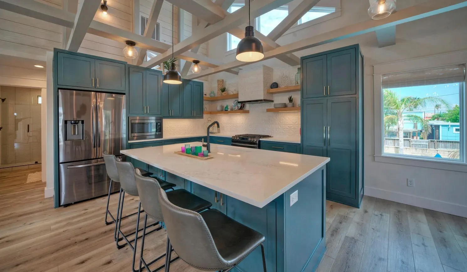 A bright kitchen with dark teal cabinets, a large island, and bar seating.