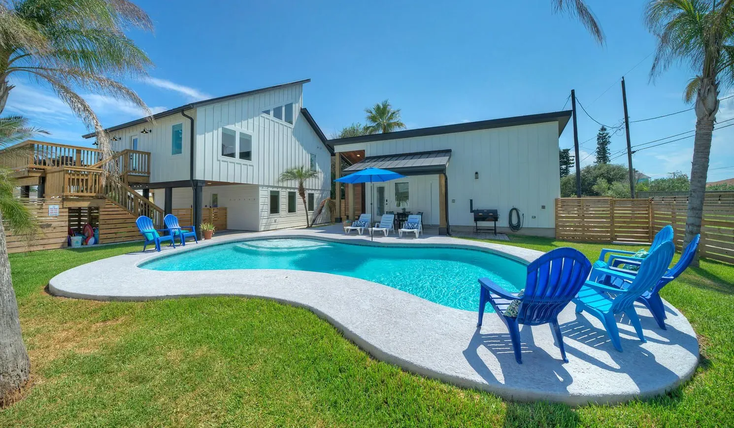 An outdoor swimming pool beside a house, with blue seating on the deck.