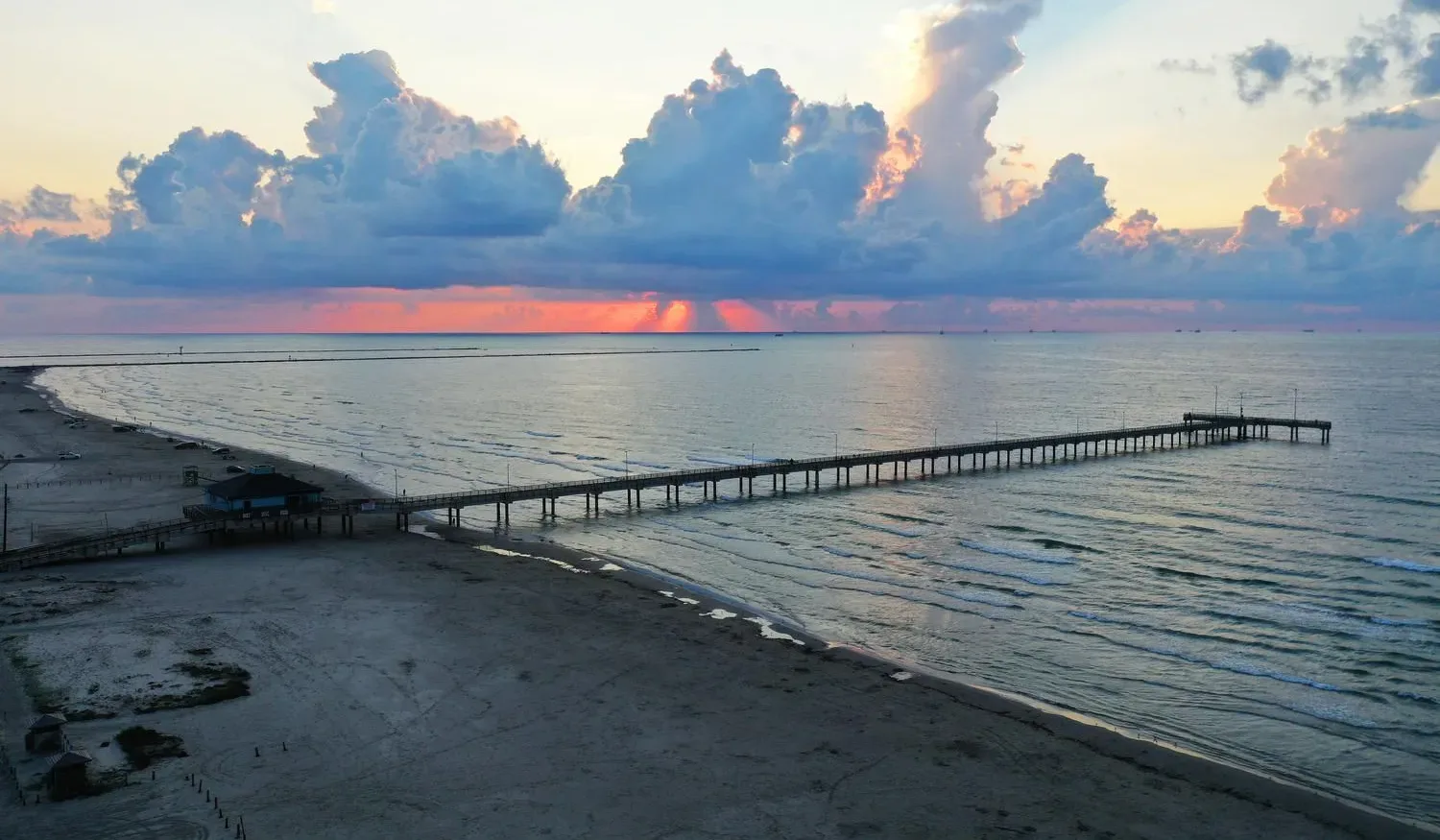 A wooden pier extends over calm water beneath a colorful sunset sky.