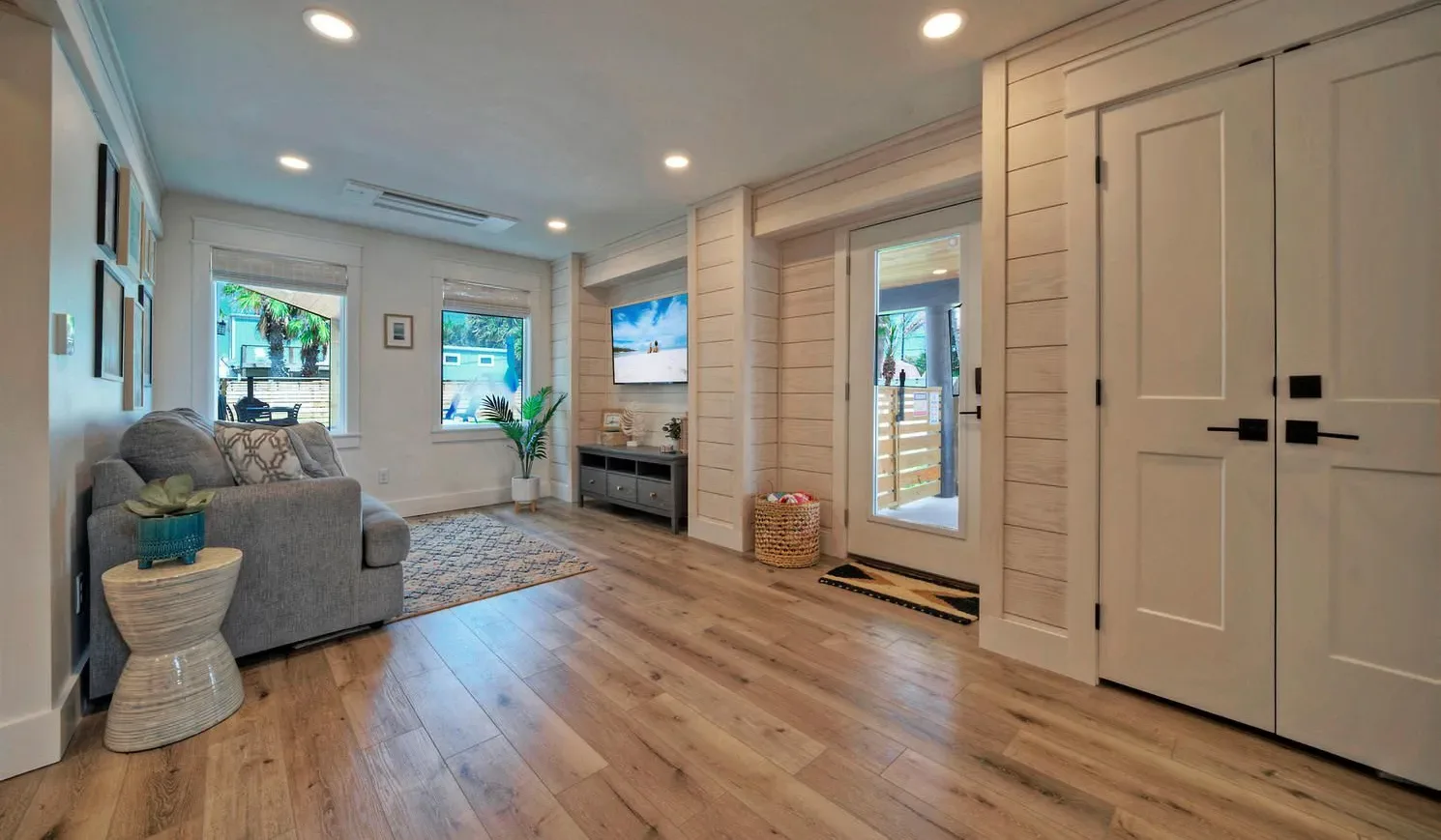 A bright living room with seating, windows, and a glass-paneled exterior door.