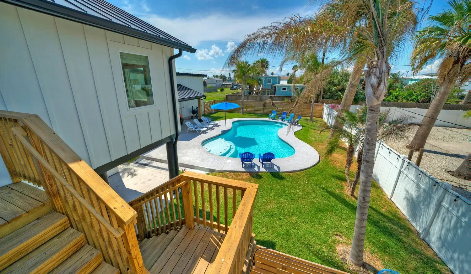 A backyard pool area with a wooden deck and palm trees.