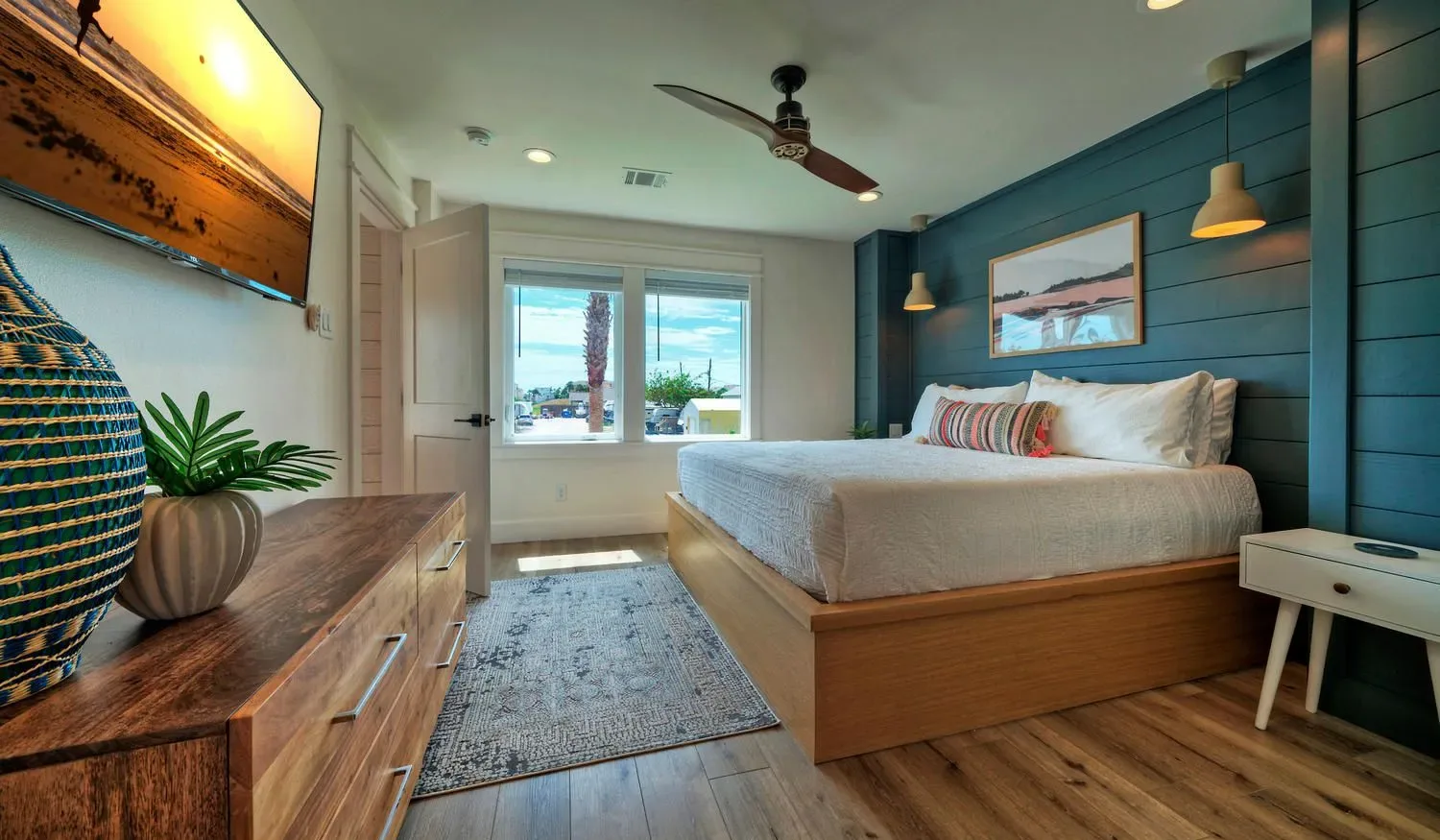 A bedroom with a large bed, a blue accent wall, and windows.