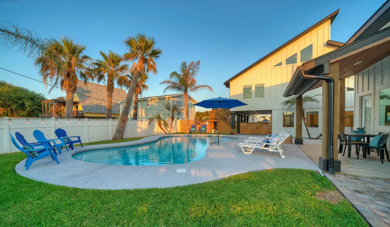 An outdoor swimming pool beside a patio with seating and palm trees.