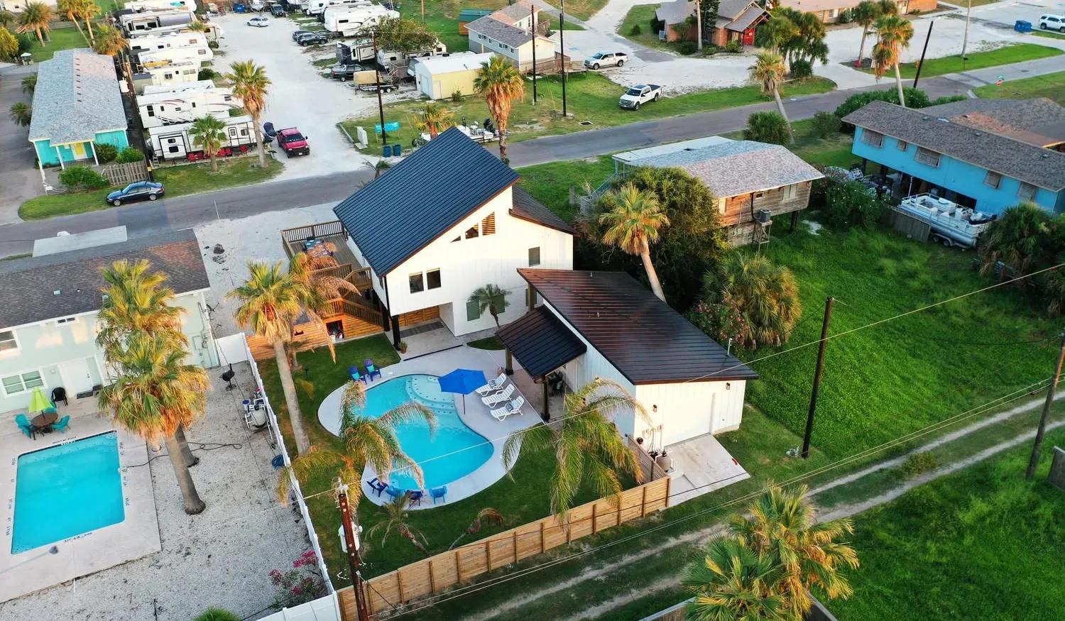 Aerial view of a house with a curved swimming pool beside a grassy lot.