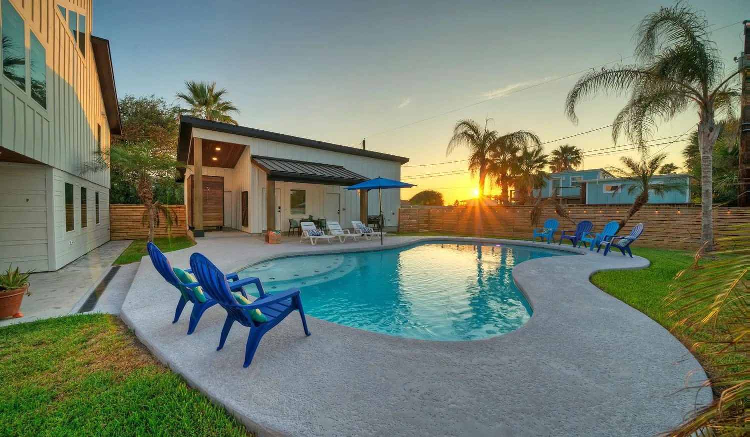 An outdoor swimming pool sits beside a modern house at sunset.