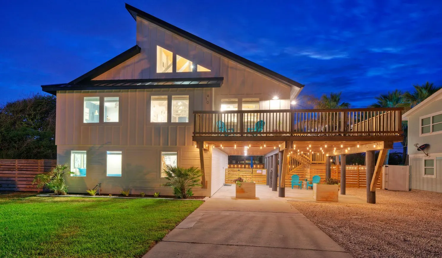 A modern two-story house glows at dusk, with a broad wooden deck above the driveway.
