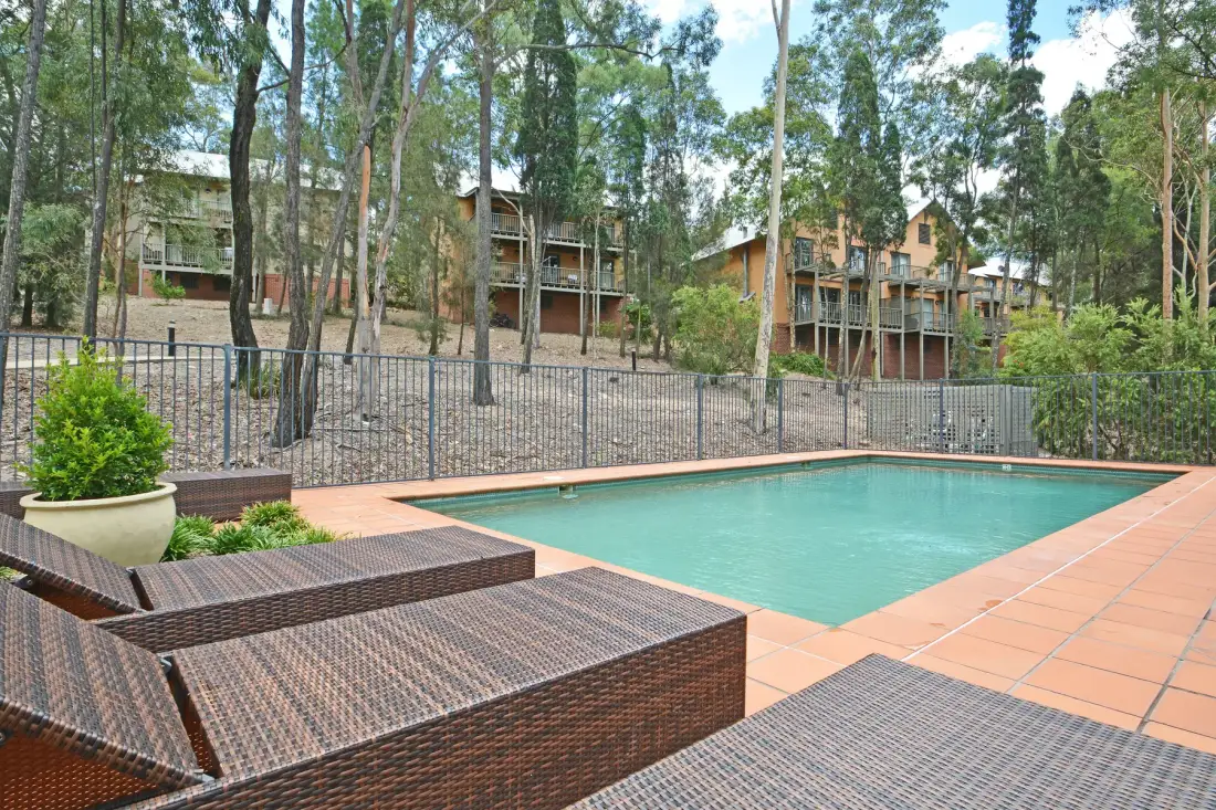 An outdoor swimming pool sits beside tiled paving and woven lounge seating.