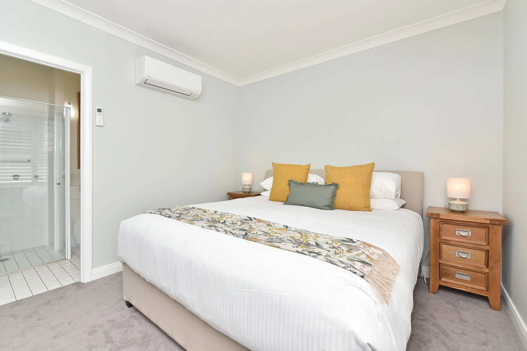 Bedroom with a neatly made bed and a bathroom visible through the open doorway.