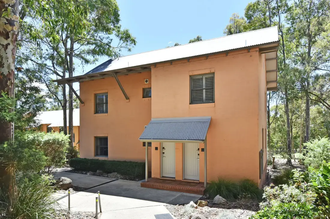 An orange building with a white roof stands among trees beside a paved walkway.