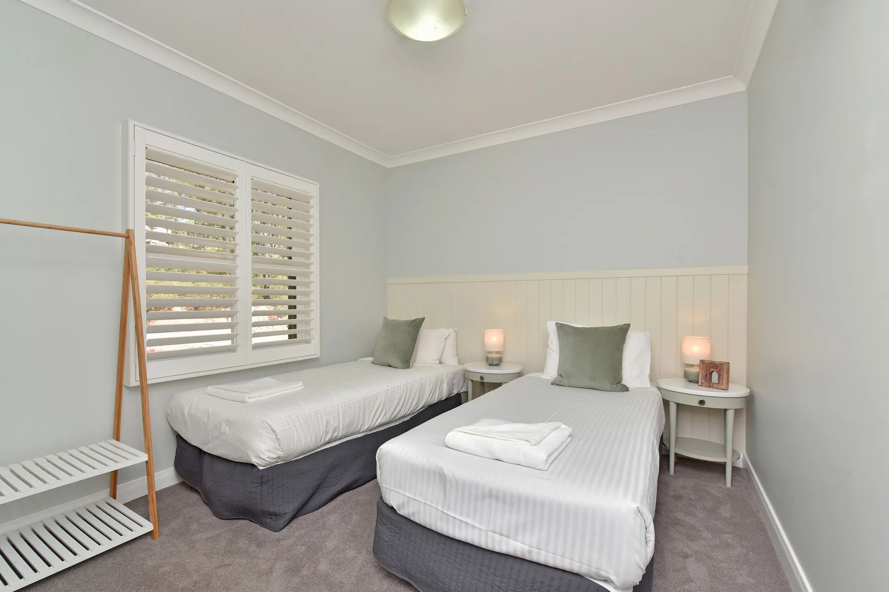 A bedroom with two beds, white bedding, and shuttered windows.