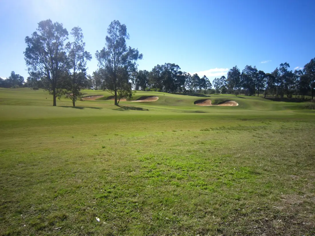Un campo de golf con calles verdes onduladas, bunkers de arena y árboles dispersos.