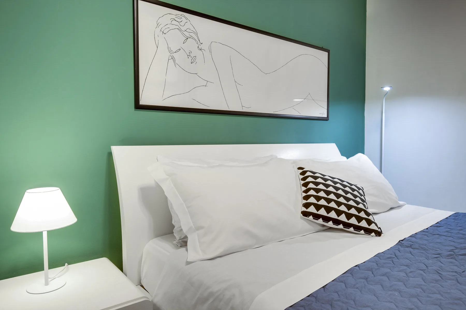 A bedroom with a neatly made bed and framed artwork on a green wall.