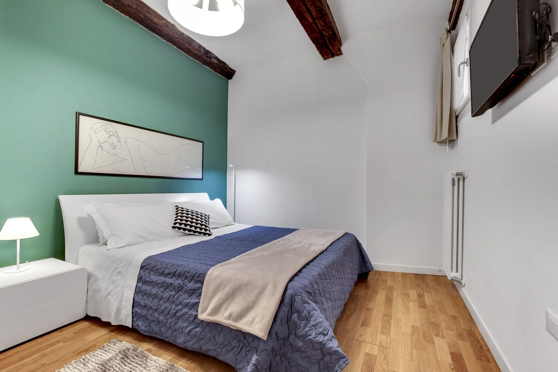 A bedroom with a bed, framed artwork, and wooden flooring.
