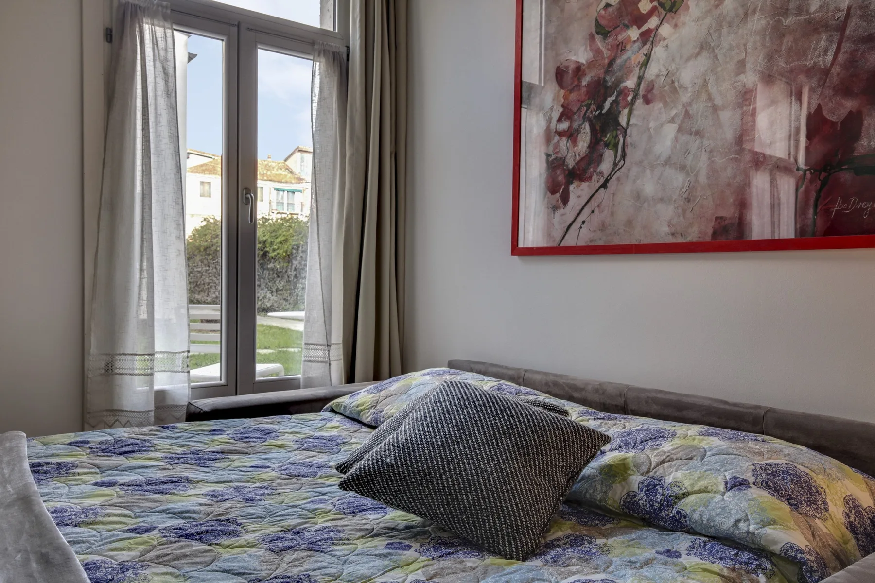 A bedroom with a patterned bedspread, pillows, and a tall window.