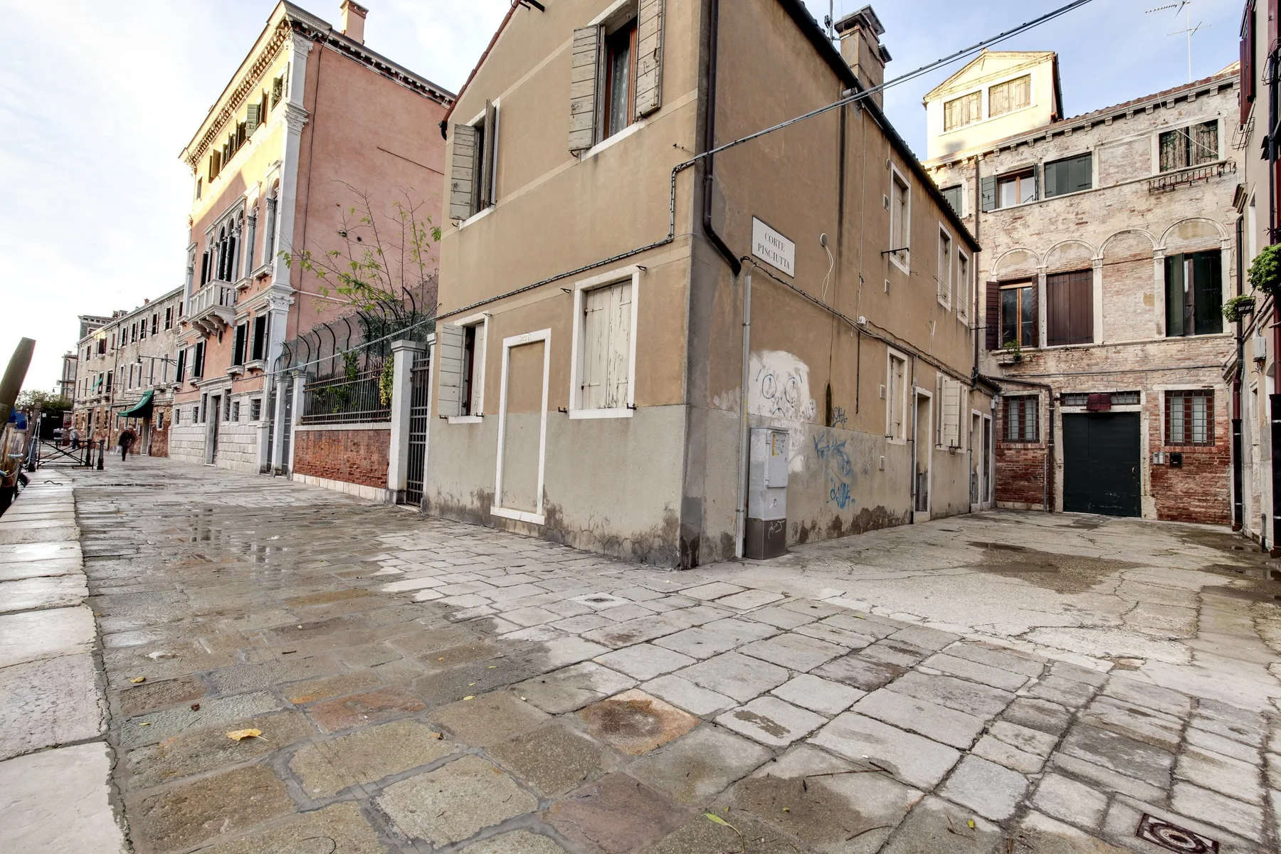 A stone-paved street runs between closely spaced buildings in an urban neighborhood.