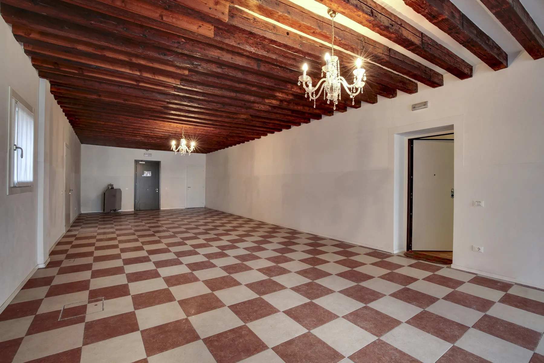 A large empty room with a checkerboard floor and exposed wooden ceiling beams.