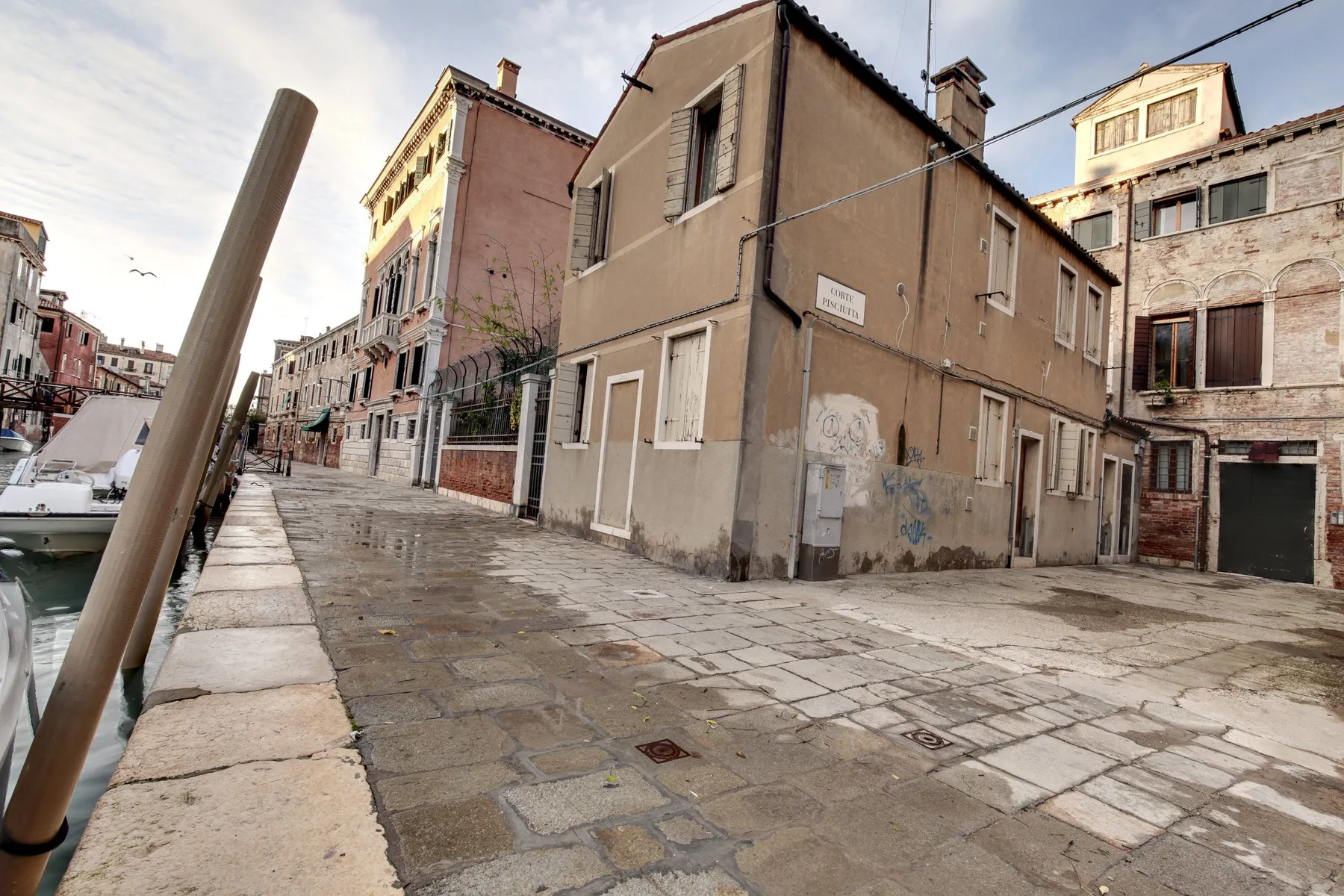 A paved canal-side street passes closely spaced historic buildings.