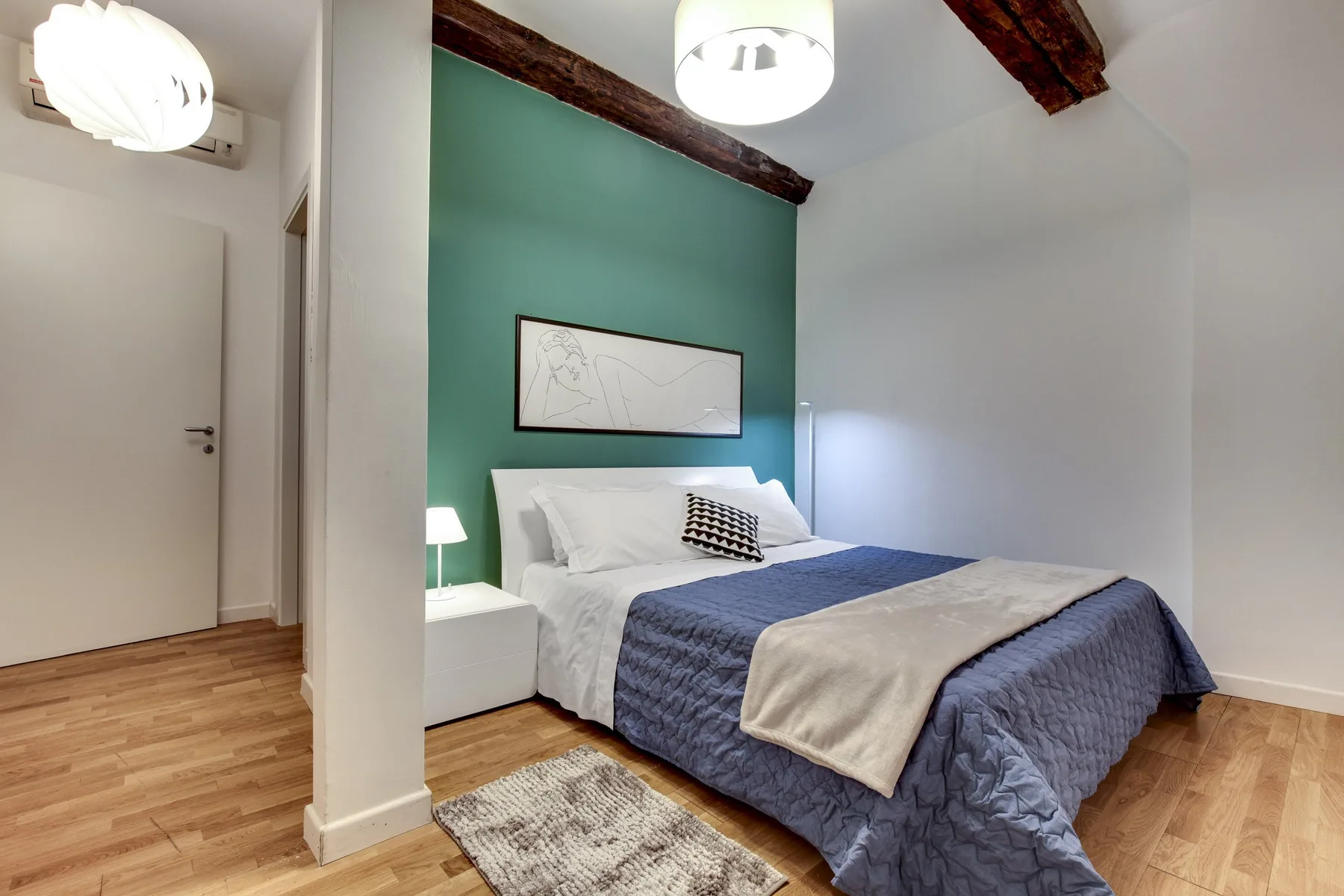 A bedroom with a bed against a green accent wall and framed artwork.