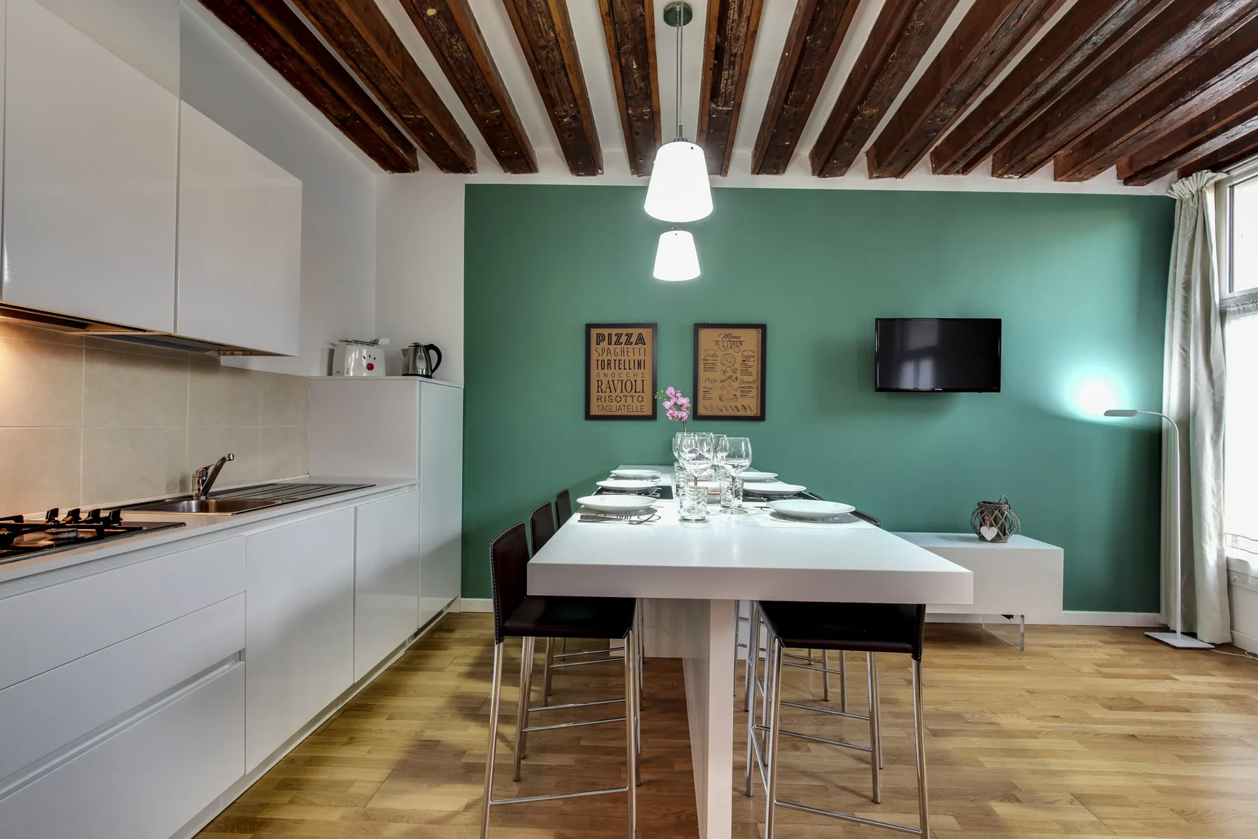 A dining area with a long table and a compact kitchen along one wall.