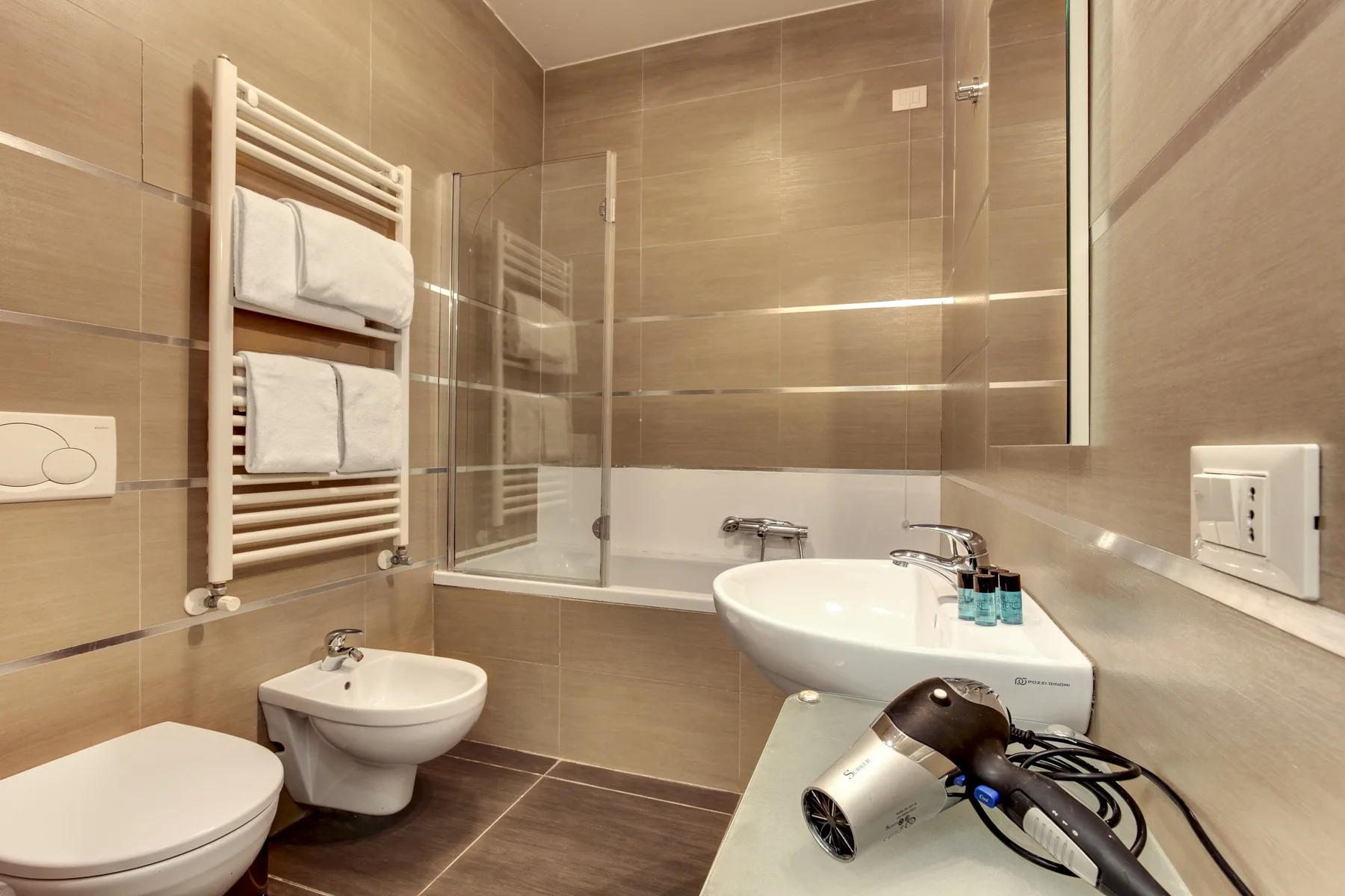 A tiled bathroom with a bathtub, sink, and towel warmer.