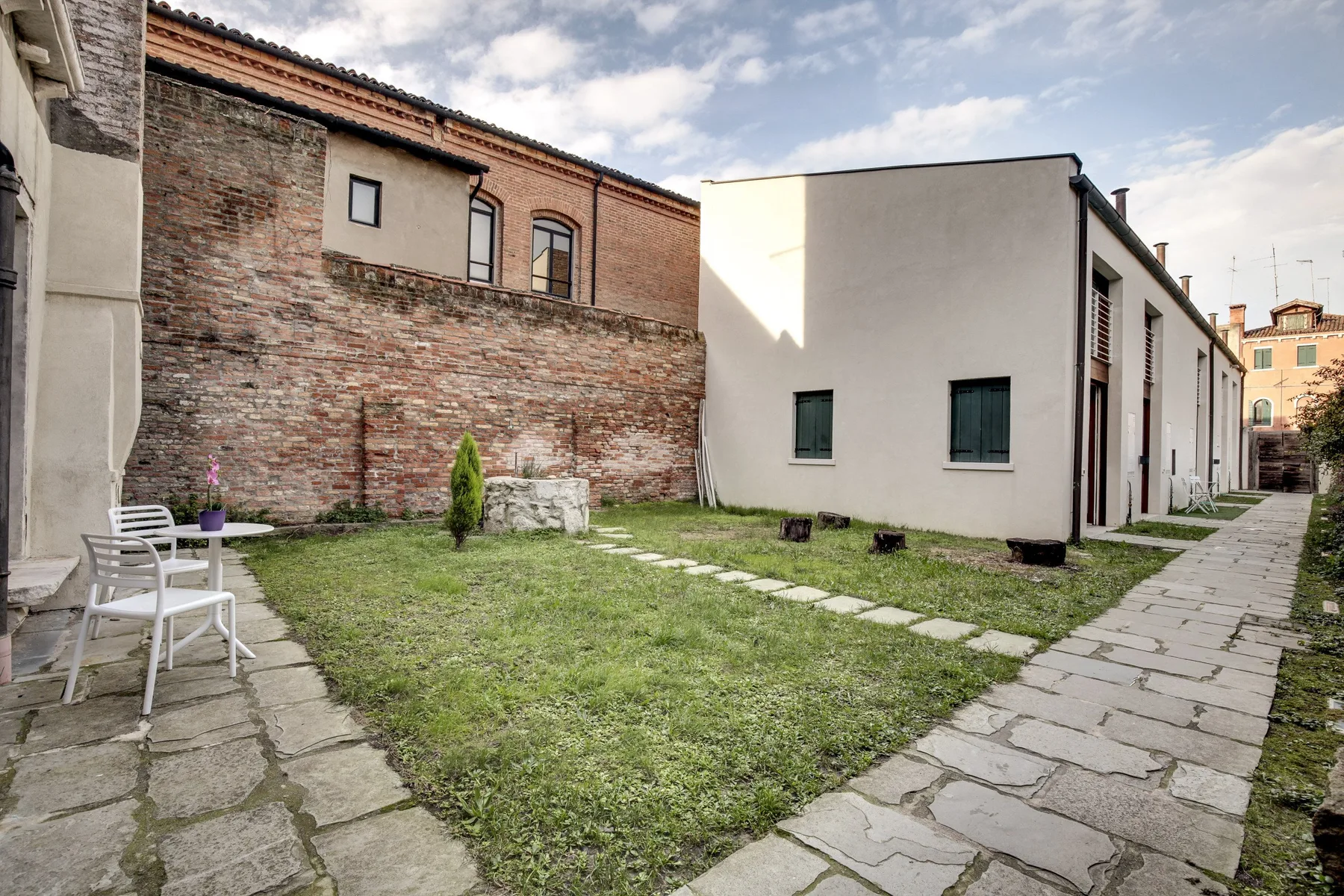 A grassy courtyard sits between brick and stucco buildings, with a stone walkway along the side.