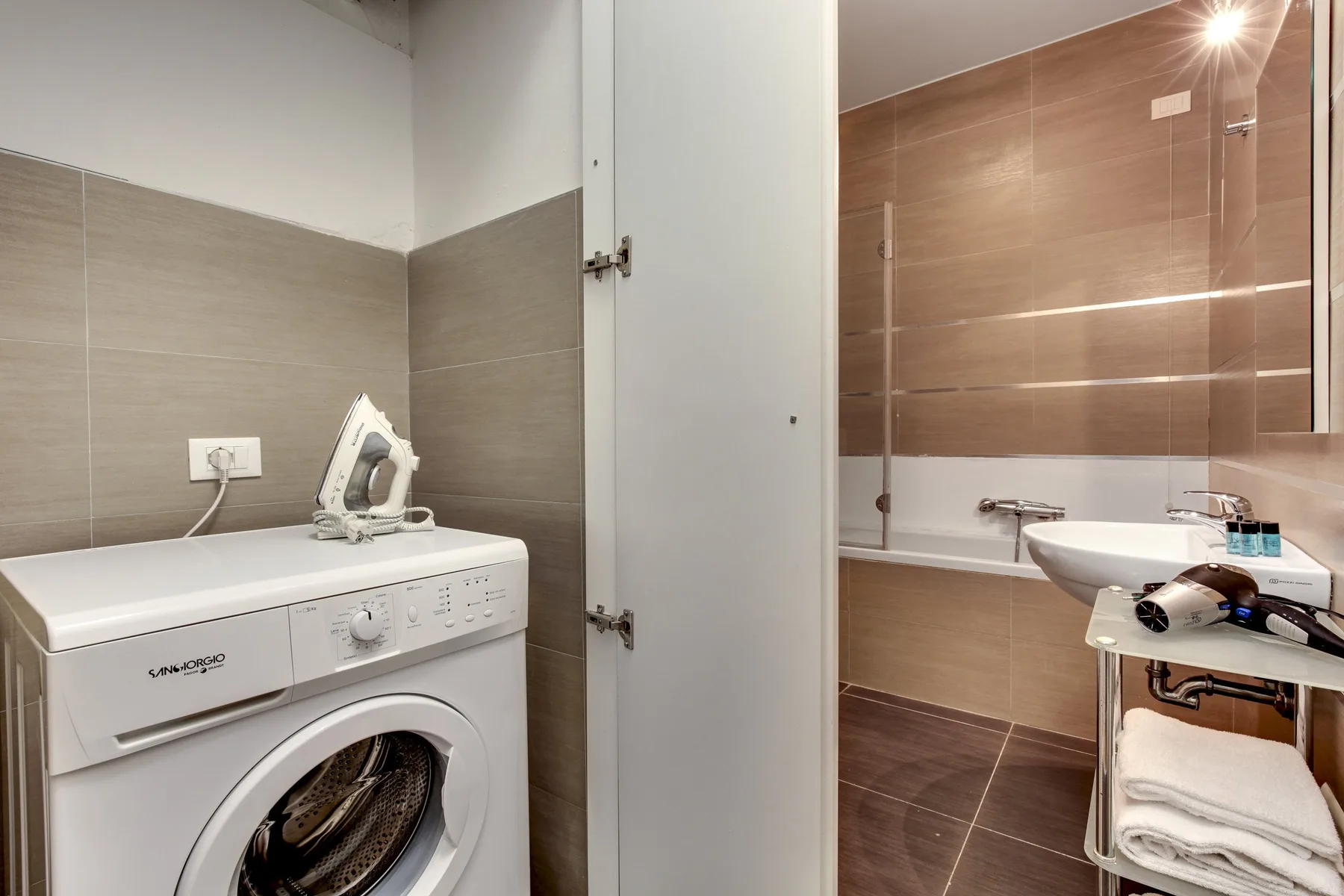 A bathroom with a washing machine and sink beside a tiled shower area.