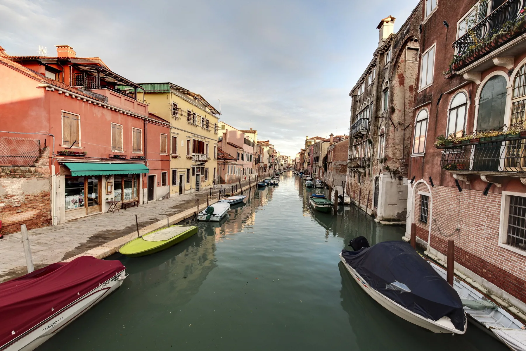 A canal runs between rows of colorful buildings, with boats moored along the water.