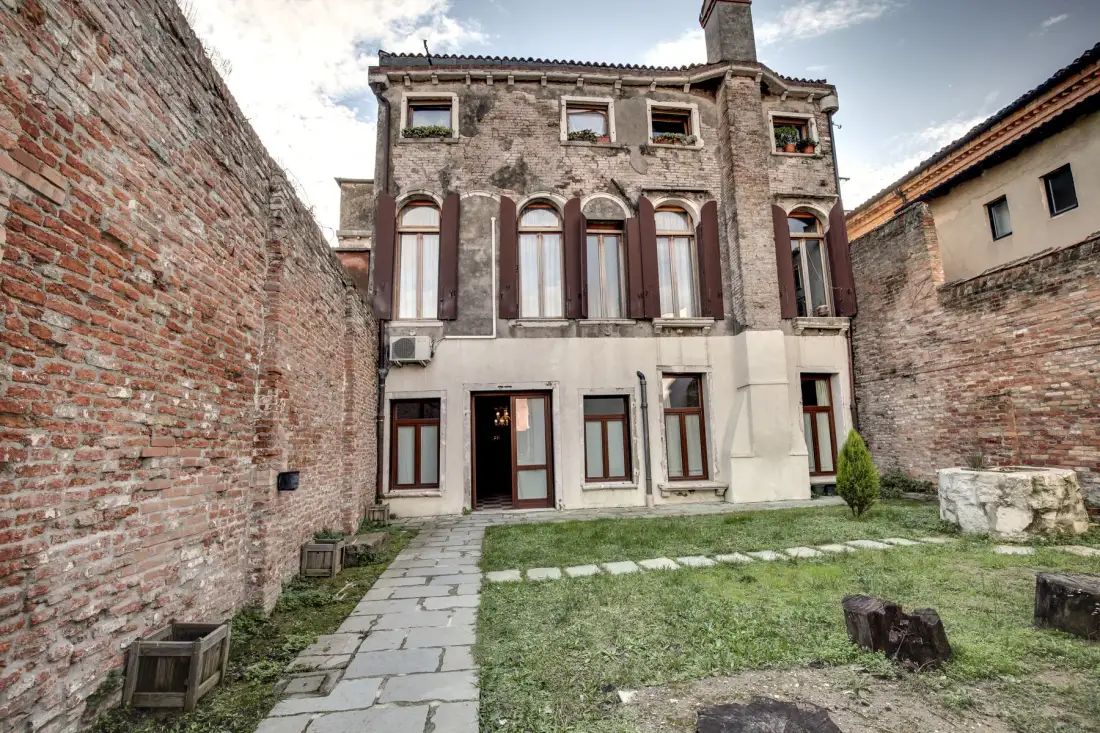 A historic-looking building faces a stone path and a small grassy courtyard.