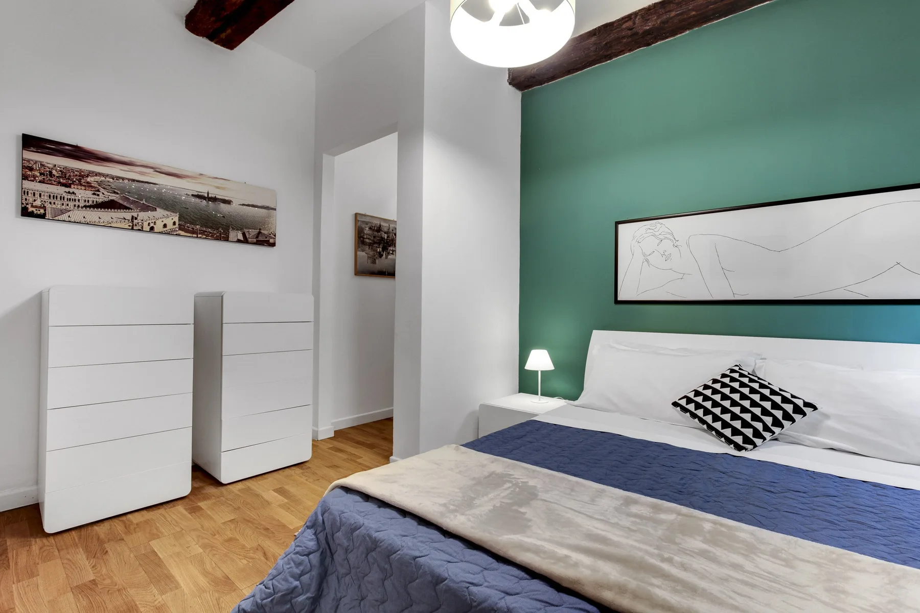 A bedroom with a bed, white dressers, and a green accent wall.