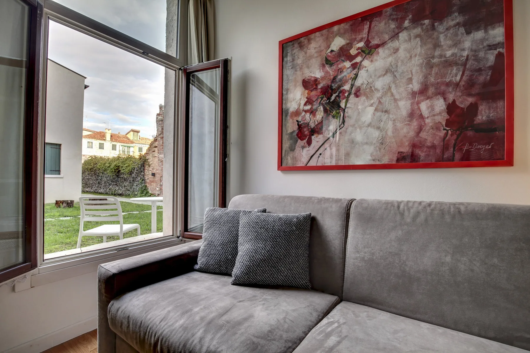 A gray seating area beside an open window, with a large abstract painting above it.