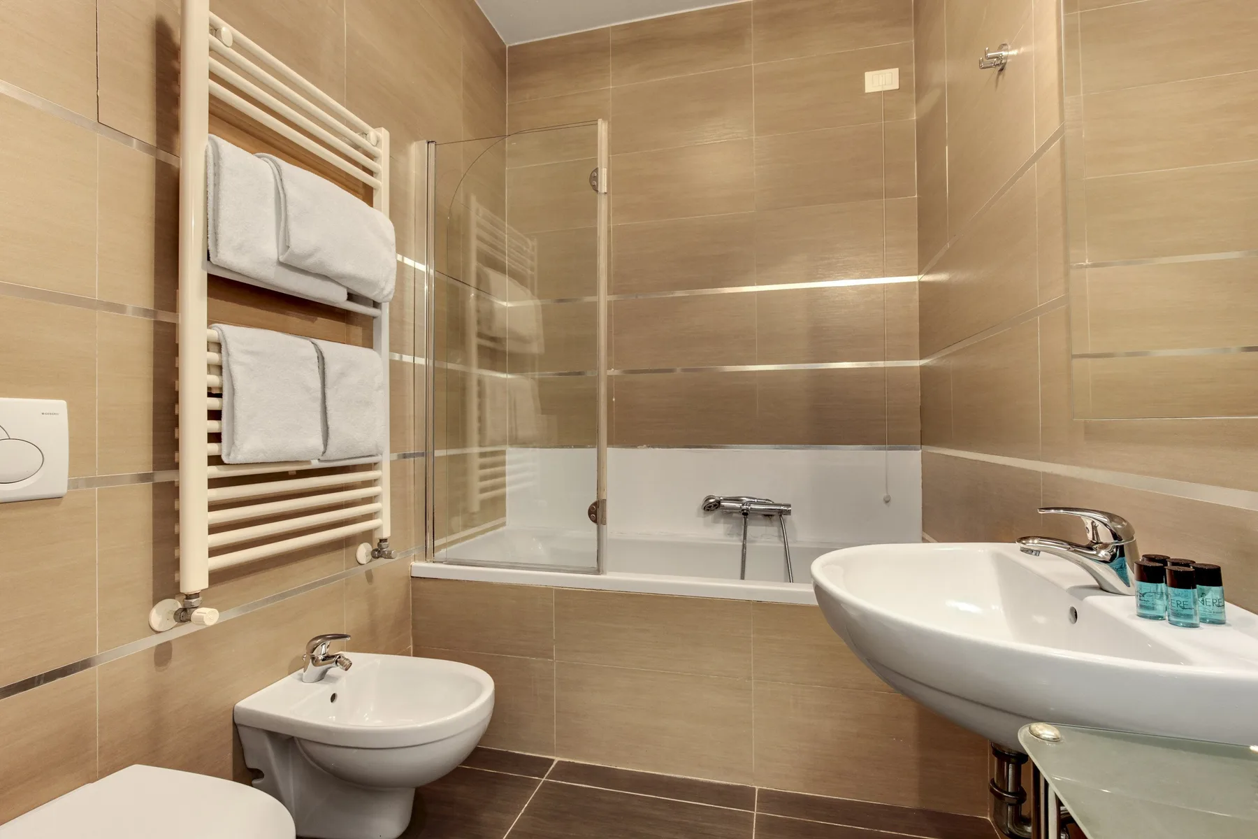 A tiled bathroom with a bathtub, wall-mounted towel warmer, and two sinks.