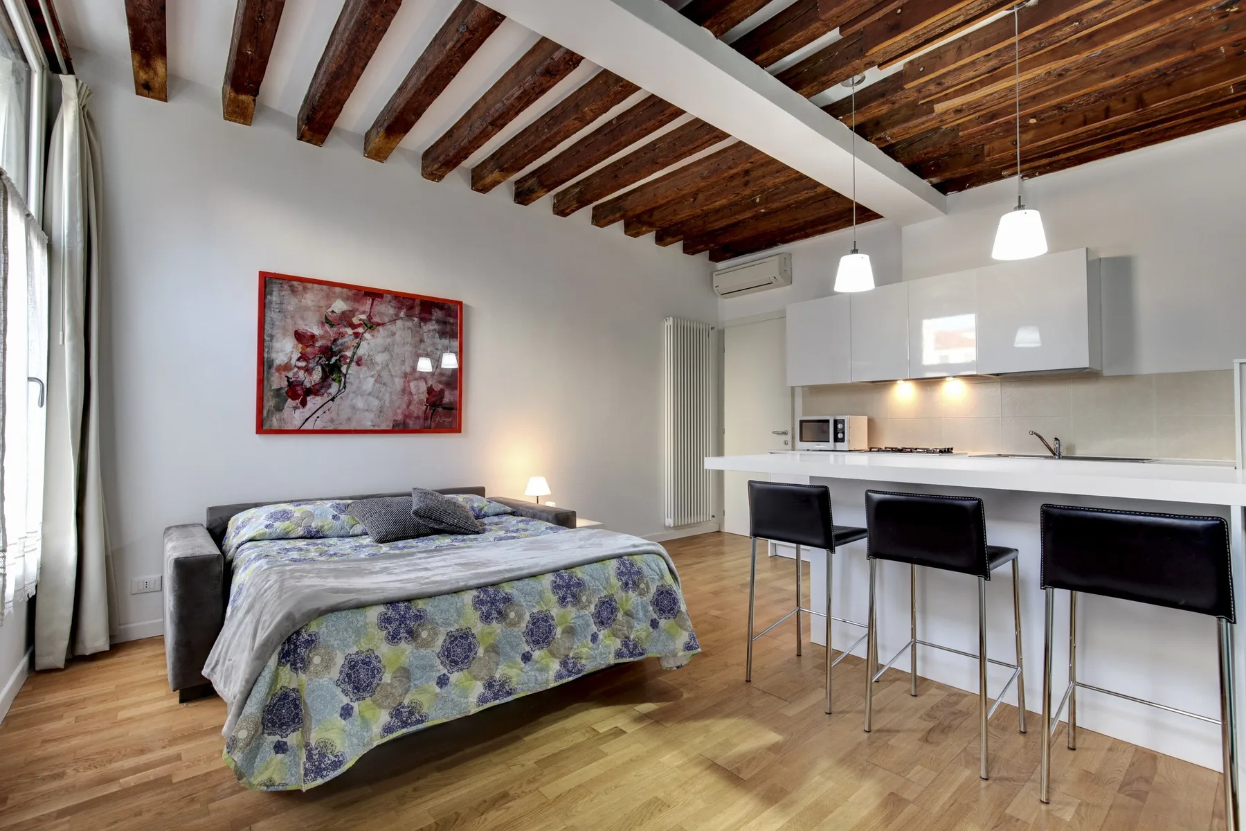 A bedroom with a bed beside a compact kitchen and counter.