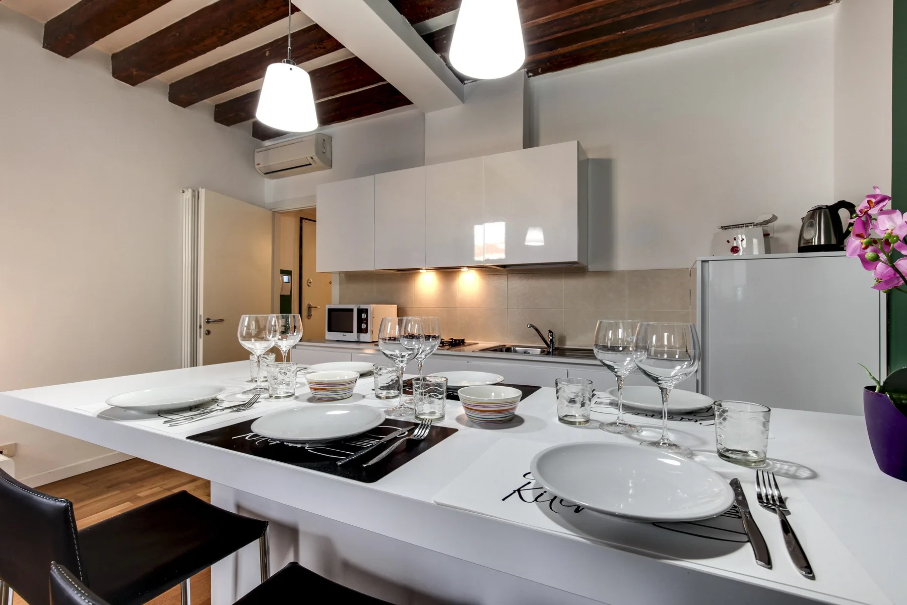 A dining table is set with plates and glasses in a kitchen.