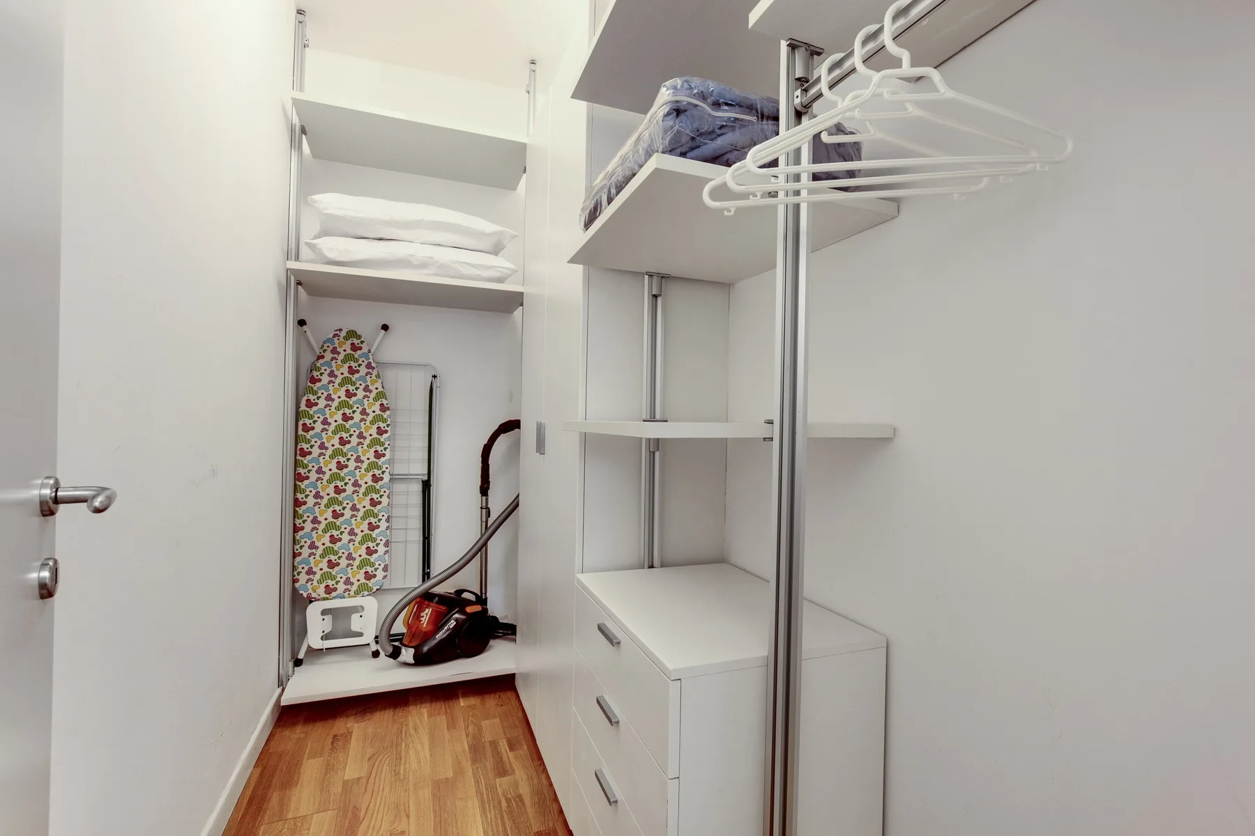 A compact dressing room with open shelving, drawers, and a clothes rail.