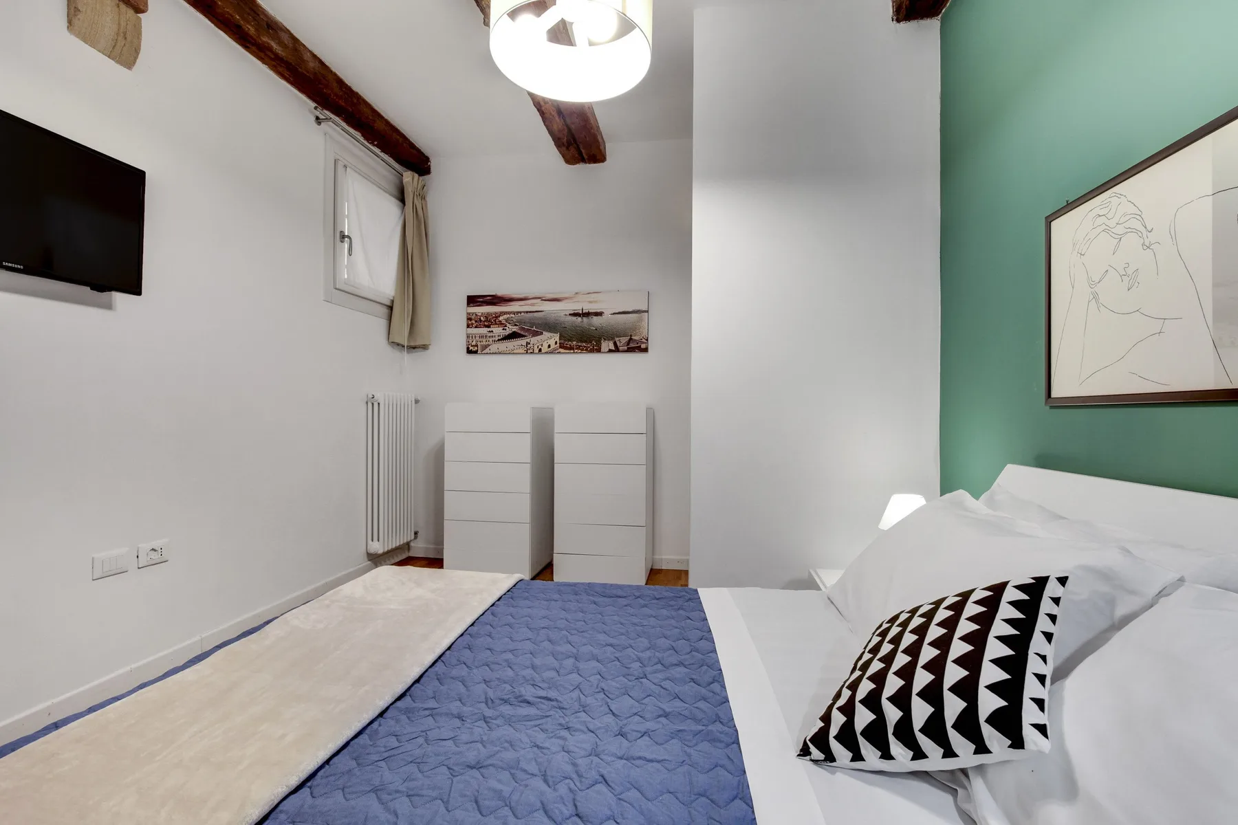 A bedroom with a bed, a wall-mounted television, and framed artwork.